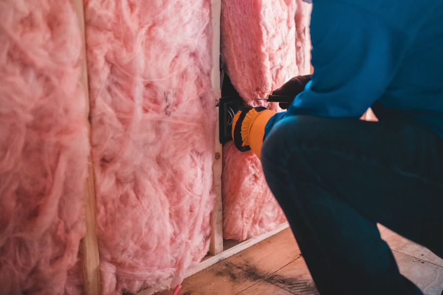 Ouvrier en gants posant de la laine de verre rose entre les montants d'une ossature de mur
