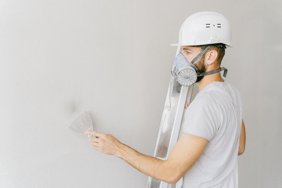 Ouvrier casqué avec masque de protection, une spatule à la main, devant un mur blanc fraîchement lissé